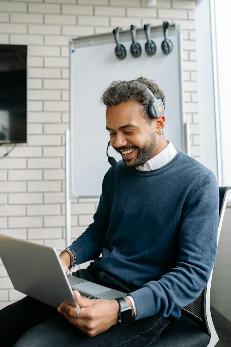 Man in Blue Sweater Smiling while Looking at the Laptop